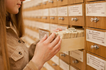 Female student looking for a specific book in old library card catalogue system. Woman browsing through retro style library book collection. Female higher education university or at public library