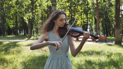 A young girl plays the violin in the city park.
