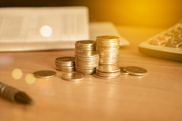 Stack of gold money coin on wood desk with calculator and pen. Business and financial concept. 