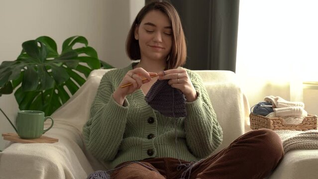 Pretty young woman holding crochet hook , enjoy knitting , sit on sofa. Smiling girl knits handmade scarf at home, lady handwork craft hobby concept, portrait. 4k footage