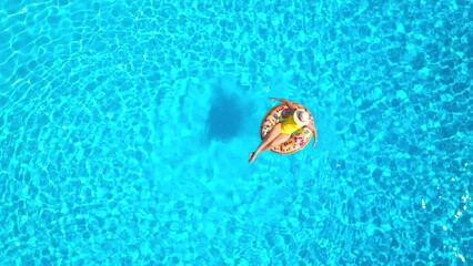 Aerial view of a woman in yellow swimsuit lying on a donut in the pool