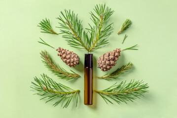 Bottle of oil and cones and needles of conifers trees on a green background