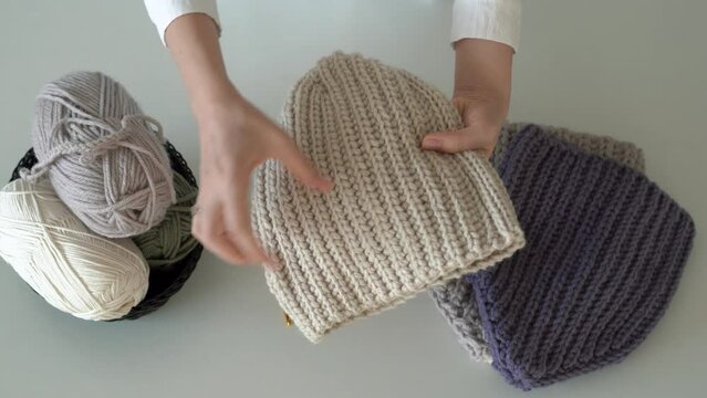 Video tutorial about how to crochet woolen clothes . Female hands show knitted hats over white table. Social media. Top view. 4k footage