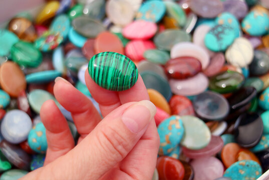 Closeup of woman's hand picking a Malachite stone with blurrry semi precious stones pile in background