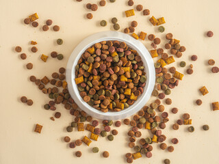 Dry pet food in a white plastic bowl top view. Pieces of food are spilled on the table