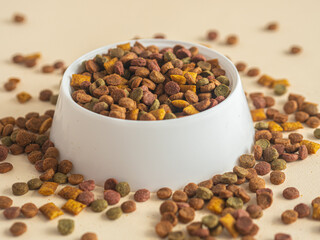 Dry pet food in a white plastic bowl. Pieces of food are spilled on the table
