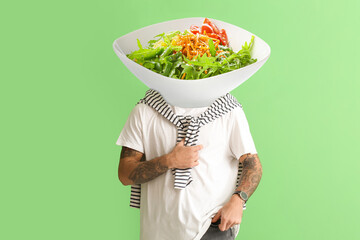 Tattooed man with plate of tasty Caesar salad instead of his head on green background