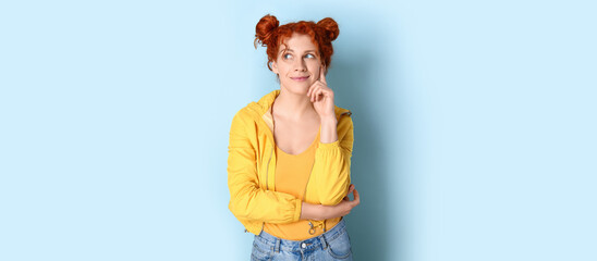 Pretty thoughtful redhead woman on light blue background