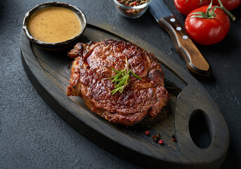 Fresh juicy delicious beef steak served on wooden cutting board over black background. Meat dish with spices and herbs