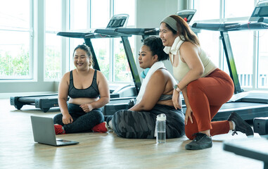 Group of overweight girls watching yoga tape together with laptop to practice yoga in the gym.Relationship and fat girl exercising concept - obrazy, fototapety, plakaty