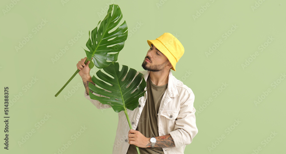 Poster Fashionable young man with tropical monstera leaves on green background