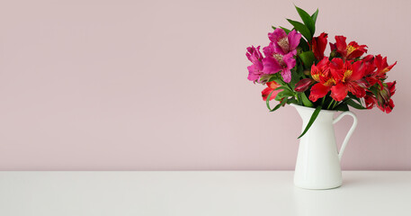 Vase with bouquet of beautiful alstroemeria flowers on table near light wall. Banner for design