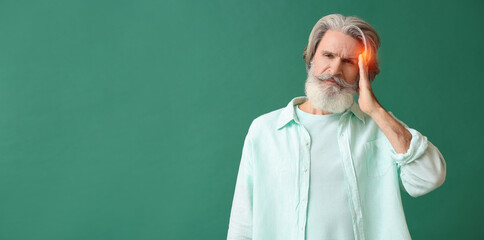 Mature man suffering from headache on green background with space for text