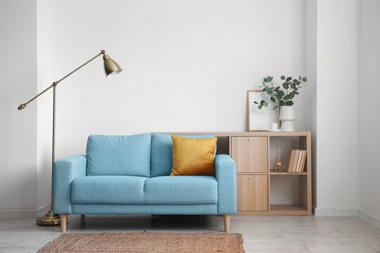 Interior of light living room with blue sofa, lamp and shelving unit