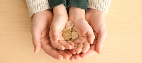 Hands of man and his son holding coins on wooden background. Concept of alimony