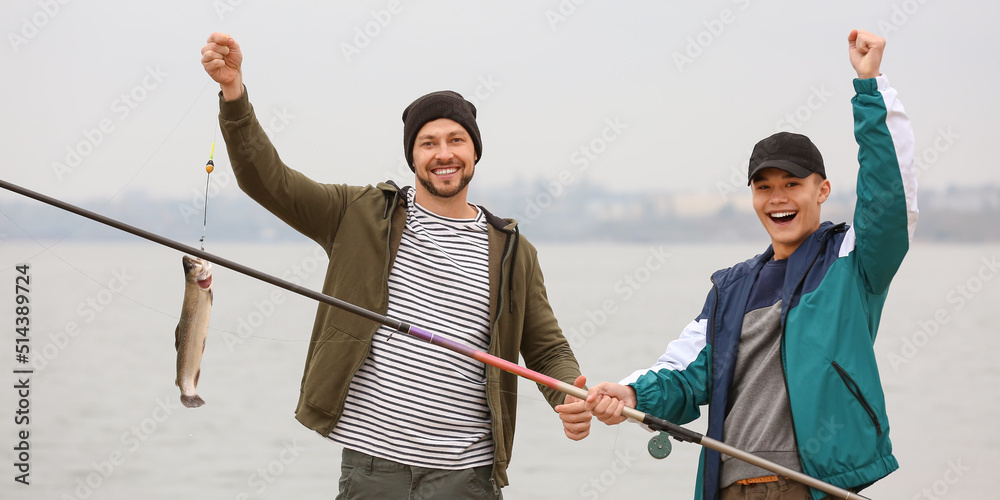 Poster happy father and son with caught fish on river bank