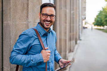 Portrait of happy professional with digital tablet leaning against wall in the city