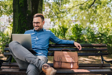 Confident smiling professional analyzing business plan on laptop at park bench
