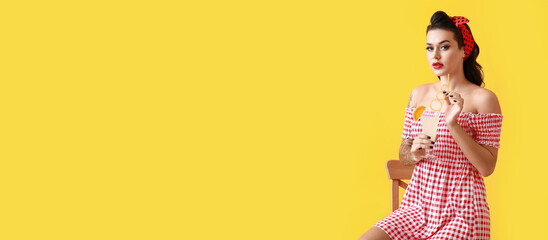 Portrait of beautiful tattooed pin-up woman with cocktail on yellow background with space for text