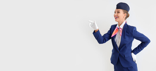 Beautiful stewardess pointing at something on light background with space for text
