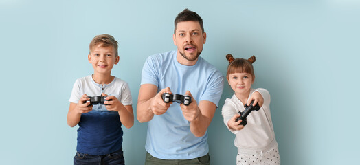 Father and his little children playing video games on light blue background
