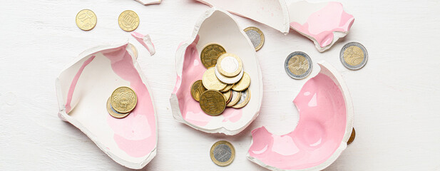 Broken piggy bank with coins on white wooden background