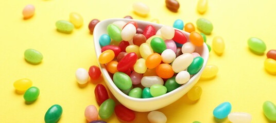 Bowl with different sweet candies on yellow background
