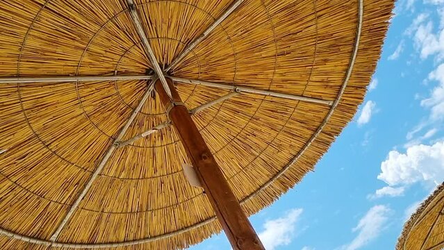 Under the reed straw beach umbrella and clear blue sky on a sunny day. Low angle rotates shot. Straw Parasol. Thatched umbrella.