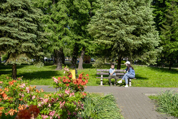 woman with kid sitting on the bench at public park. boy eating ice cream