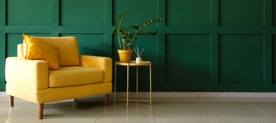 Cozy yellow armchair with table near green wall with space for text