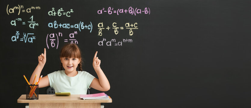 Cute schoolgirl sitting at desk during maths lesson in classroom