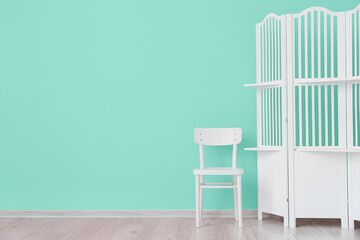 White folding screen and empty chair near mint wall in room interior