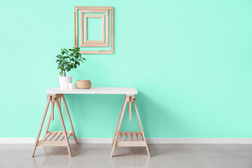 Stylish table with houseplant and decor near mint wall in room interior