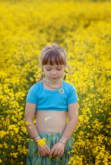 Pretty little girl walking with blue dress in boho style in rapeseed field. Cute young lady model in summer sunny day.
