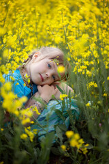Portrait of a cute girl kid in a yellow rape flower field. A child in a blooming meadow. Authenticity, rural life, eco-friendly