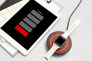 Smartwatch charging with wireless pad and uncharged tablet computer on grey background, closeup