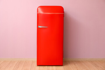 Stylish retro fridge near pink wall in room