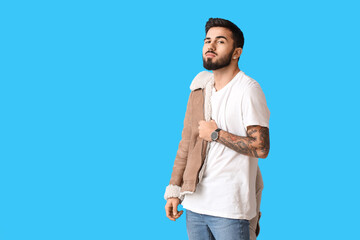 Naklejka premium Fashionable bearded man with stylish winter jacket on blue background