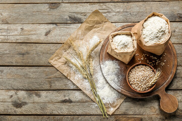 Wheat ears, bowl, paper bags with flour, board and parchment paper on wooden background