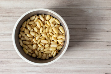 a bowl of untoasted pine nut kernels in a bowl on wooden background 