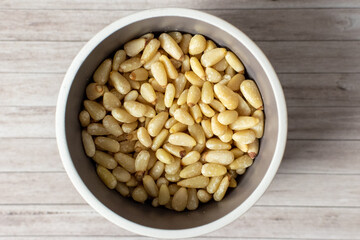 a bowl of untoasted pine nut kernels in a bowl on wooden background 