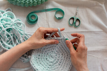 Women's hands crocheting a bag from knitted yarn. Flatley from scissors, centimeter, hook, yarn. The concept of creating a bag from knitted yarn. - obrazy, fototapety, plakaty