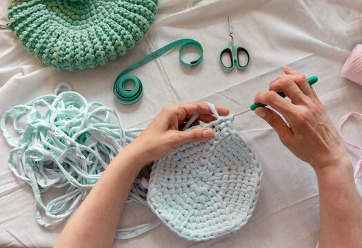 Women's hands crocheting a bag from knitted yarn. Flatley from scissors, centimeter, hook, yarn. The concept of creating a bag from knitted yarn.
