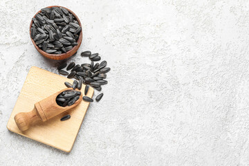 Bowl, board and scoop with black sunflower seeds on light background