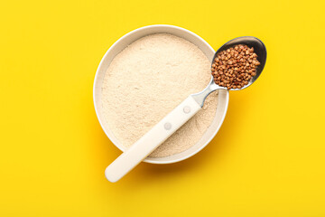 Bowl of flour and spoon with buckwheat grains on yellow background