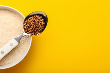 Bowl of flour and spoon with buckwheat grains on yellow background