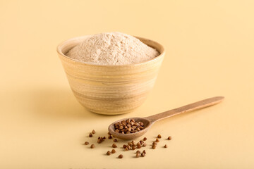 Bowl of flour and spoon with buckwheat grains on beige background