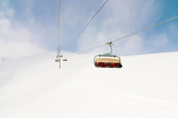 An open-air lift that goes to the top of the mountain for downhill skiing. Sunny day surrounded by snowy fields. Ski resort slope in good weather
