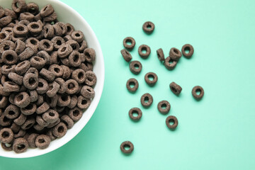 Bowl of black cereal rings on color background, closeup