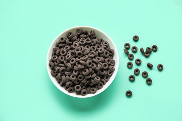 Bowl of black cereal rings on color background